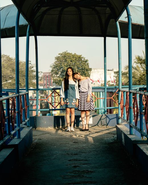 Two women standing on a colorful footbridge in daylight, expressing friendship and style.