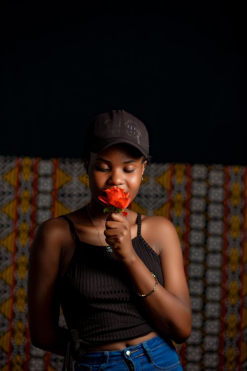 Free A young woman in a cap and tank top holds a flower with eyes closed, creating a serene fashion portrait. Stock Photo