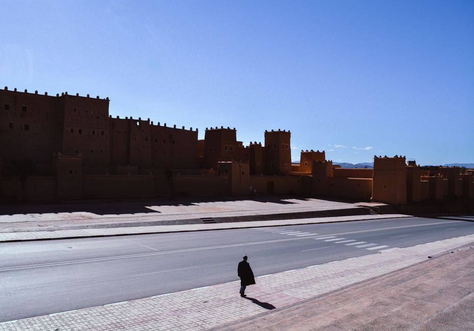Silhouette of a person walking near historic adobe walls under a clear blue sky.