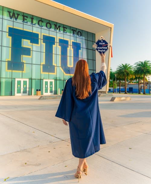 A woman in a graduation gown is standing in front of a building with the words welcome to florida