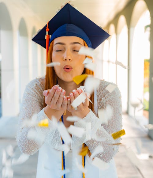 A woman in a graduation cap blowing confetti