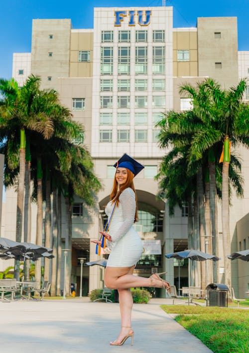 A woman in a graduation gown is posing in front of palm trees