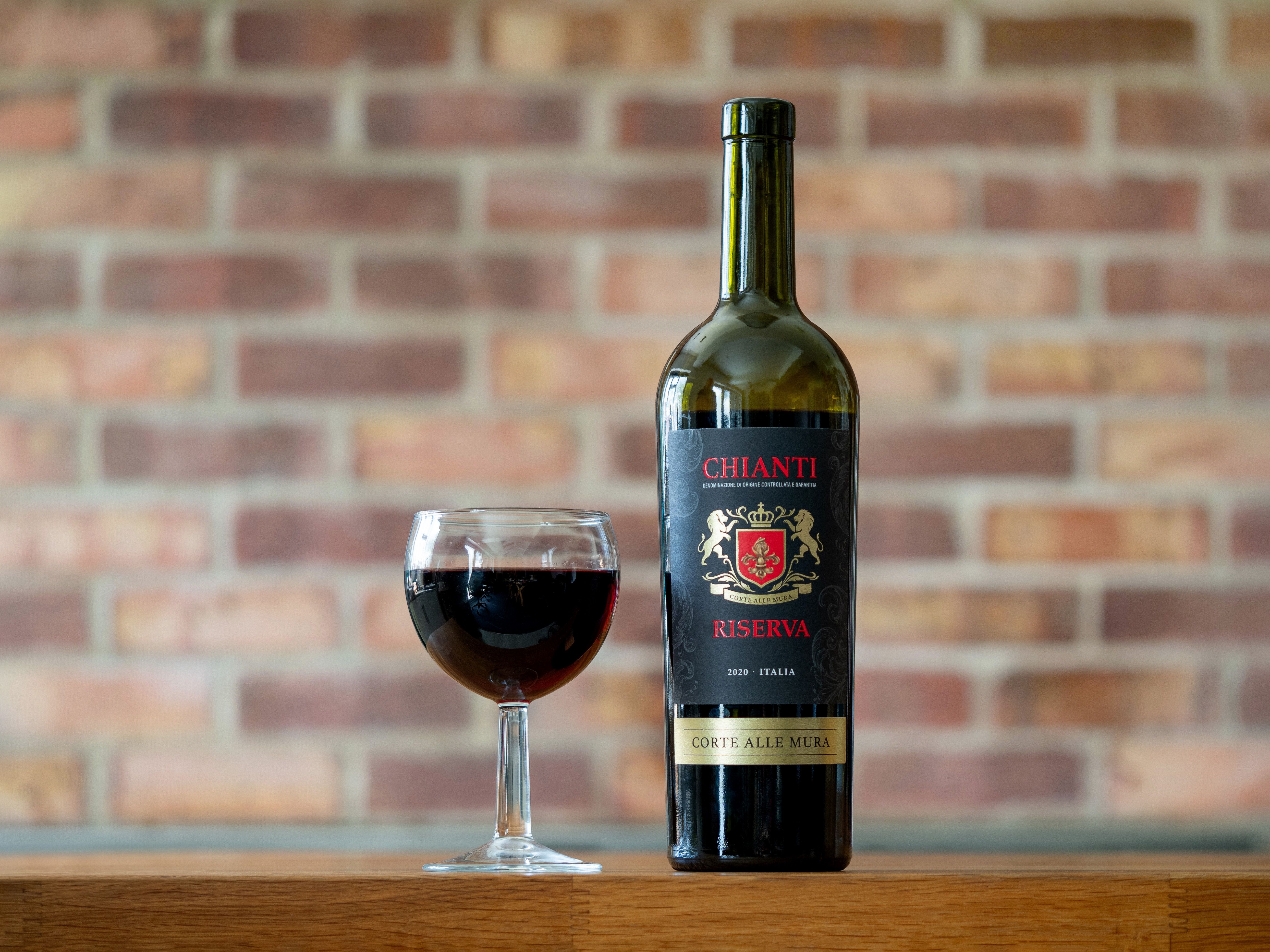 Chianti Riserva wine bottle with a filled wineglass against a brick background.