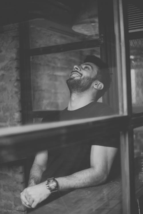 Grayscale Photography of Smiling Man Standing Beside Window