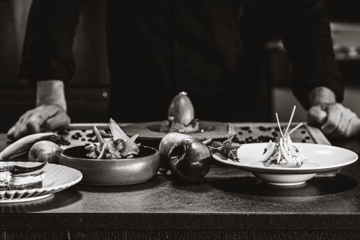 Chef arranges gourmet dishes on a table in a black and white setting.