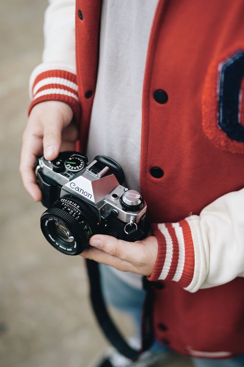 Free Close-up of a man holding a vintage camera, wearing a red and white jacket. Stock Photo