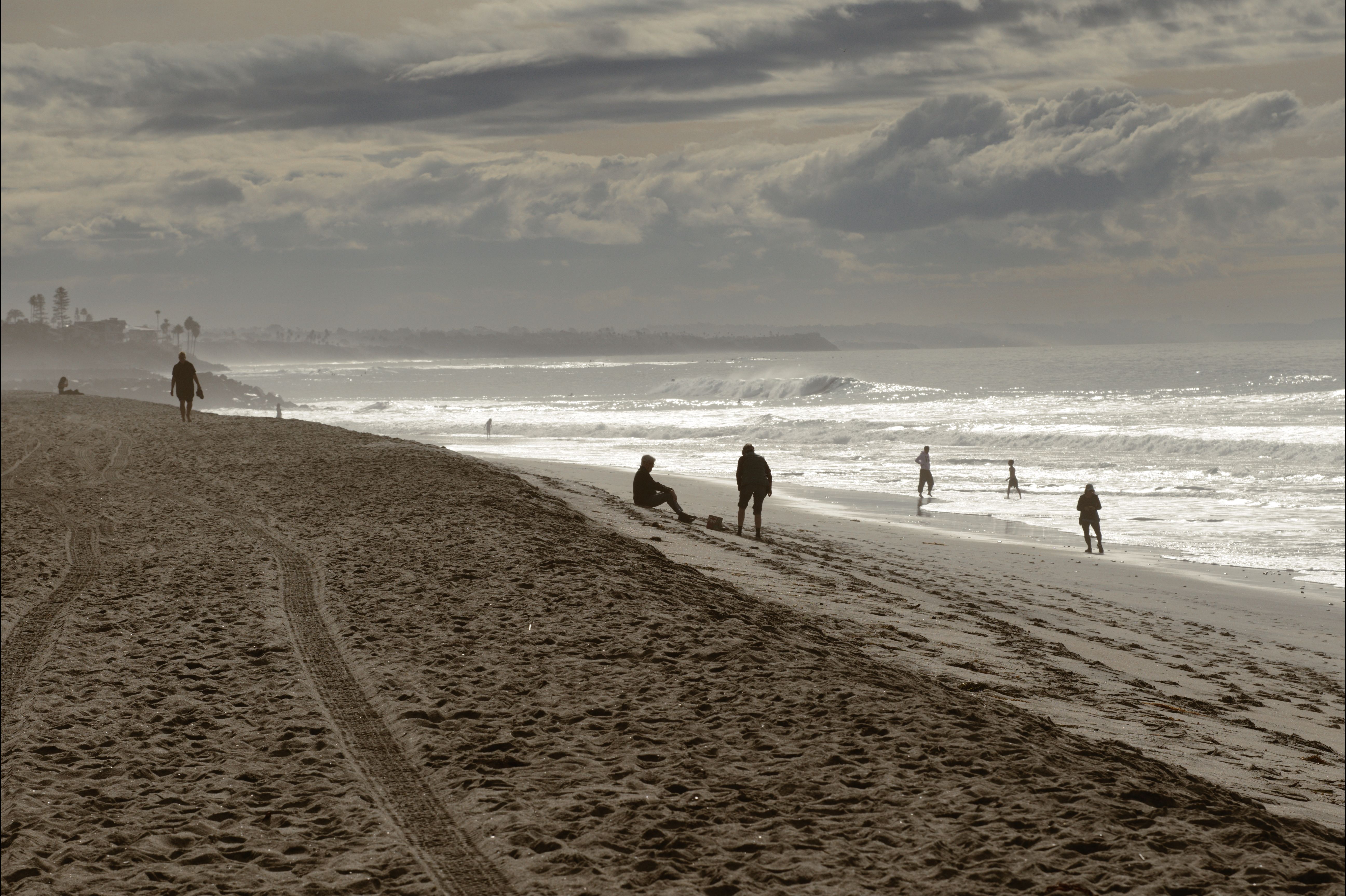 A serene beach scene in Carlsbad, CA with people walking and relaxing by the ocean under cloudy skies.