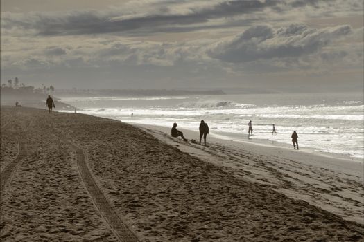A serene beach scene in Carlsbad, CA with people walking and relaxing by the ocean under cloudy skies.