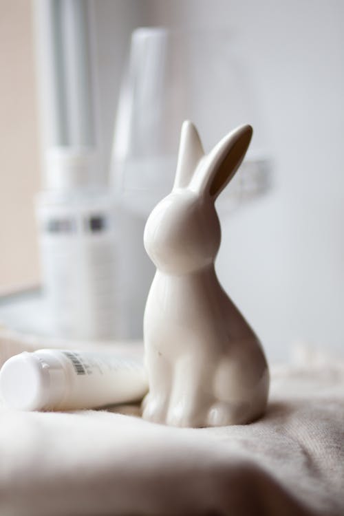 A white rabbit figurine sitting on a table next to a bottle of lotion