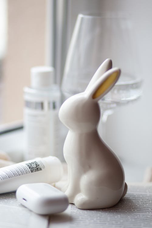 A white ceramic rabbit sitting on a table next to a bottle of lotion