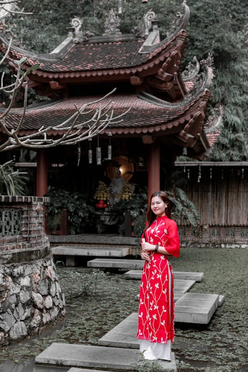 A woman in a red dress stands in front of a pagoda