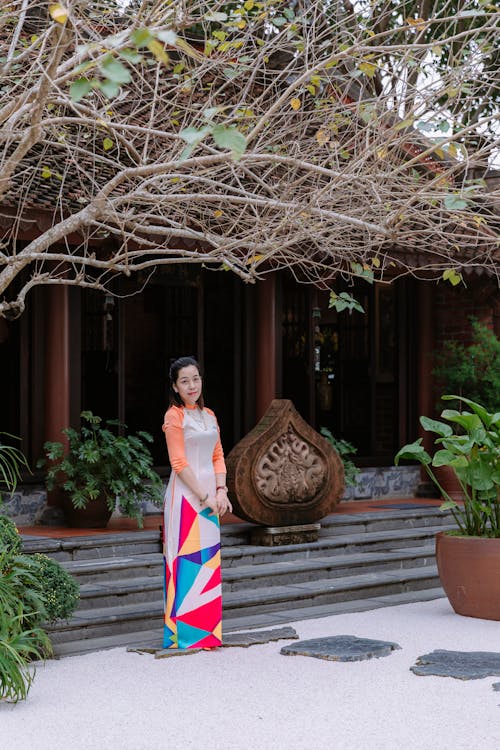 A woman in a colorful dress stands in front of a building
