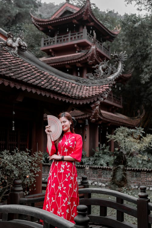 A woman in a red dress is standing in front of a pagoda