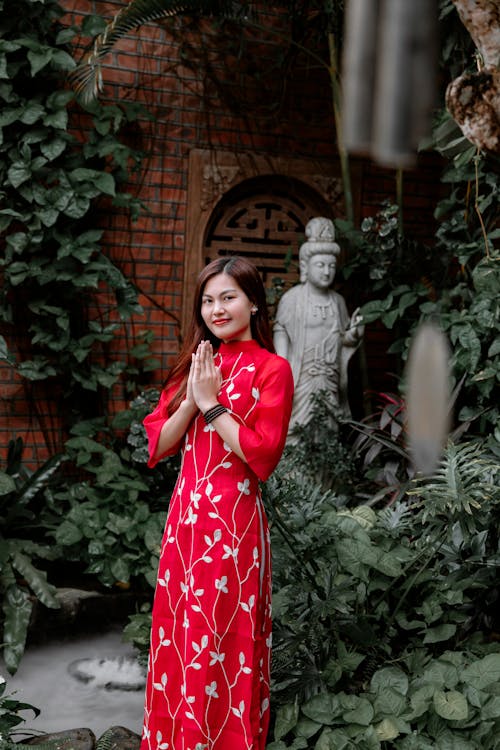 A woman in a red dress is standing in front of a garden