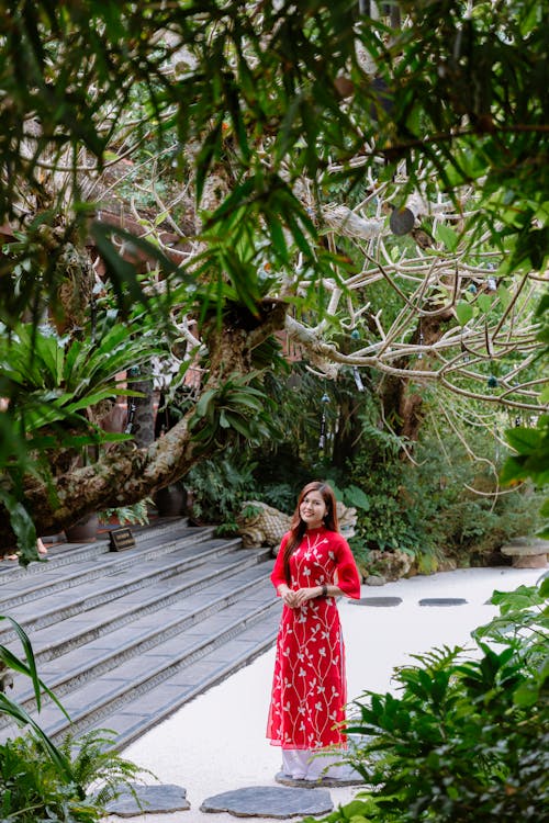 A woman in a red dress stands in front of a tree
