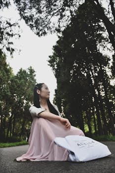 一位身穿粉色连衣裙的亚洲女子，坐在宁静森林的小路上