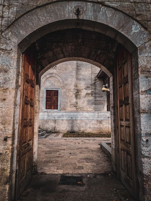 Free A serene view through a historic stone archway opening into a quiet courtyard. Stock Photo