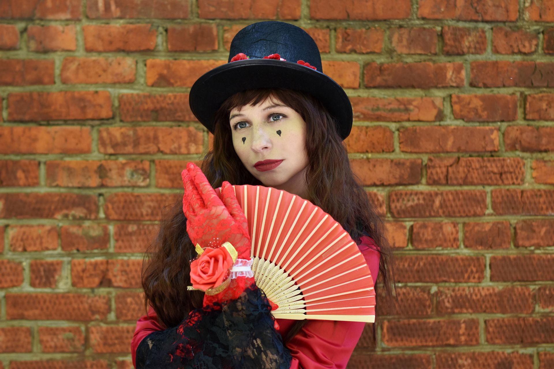 Stylish woman wearing a hat and holding a fan poses against a brick wall.