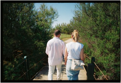 Free Back view of a couple walking hand in hand on a wooden bridge surrounded by greenery. Stock Photo
