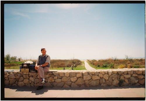 A man sitting on a stone wall with a suitcase