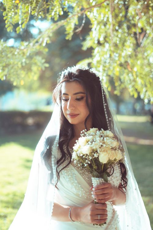 Free A beautiful bride in a white wedding dress holding a bouquet, captured in a serene garden setting in Baghdad. Stock Photo