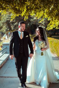 Bride and groom walking joyfully in a sunlit park in Baghdad, showcasing love and elegance.