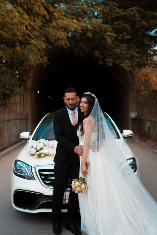 Free Newlywed couple posing by a luxury car outside a tunnel in Baghdad, Iraq. Stock Photo