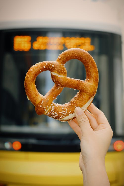 A hand holding a pretzel in front of a bus