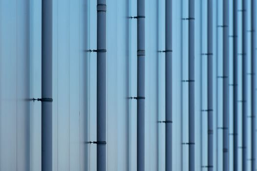 Close-up of blue metal pipes on the exterior of an industrial building, creating a symmetrical pattern.