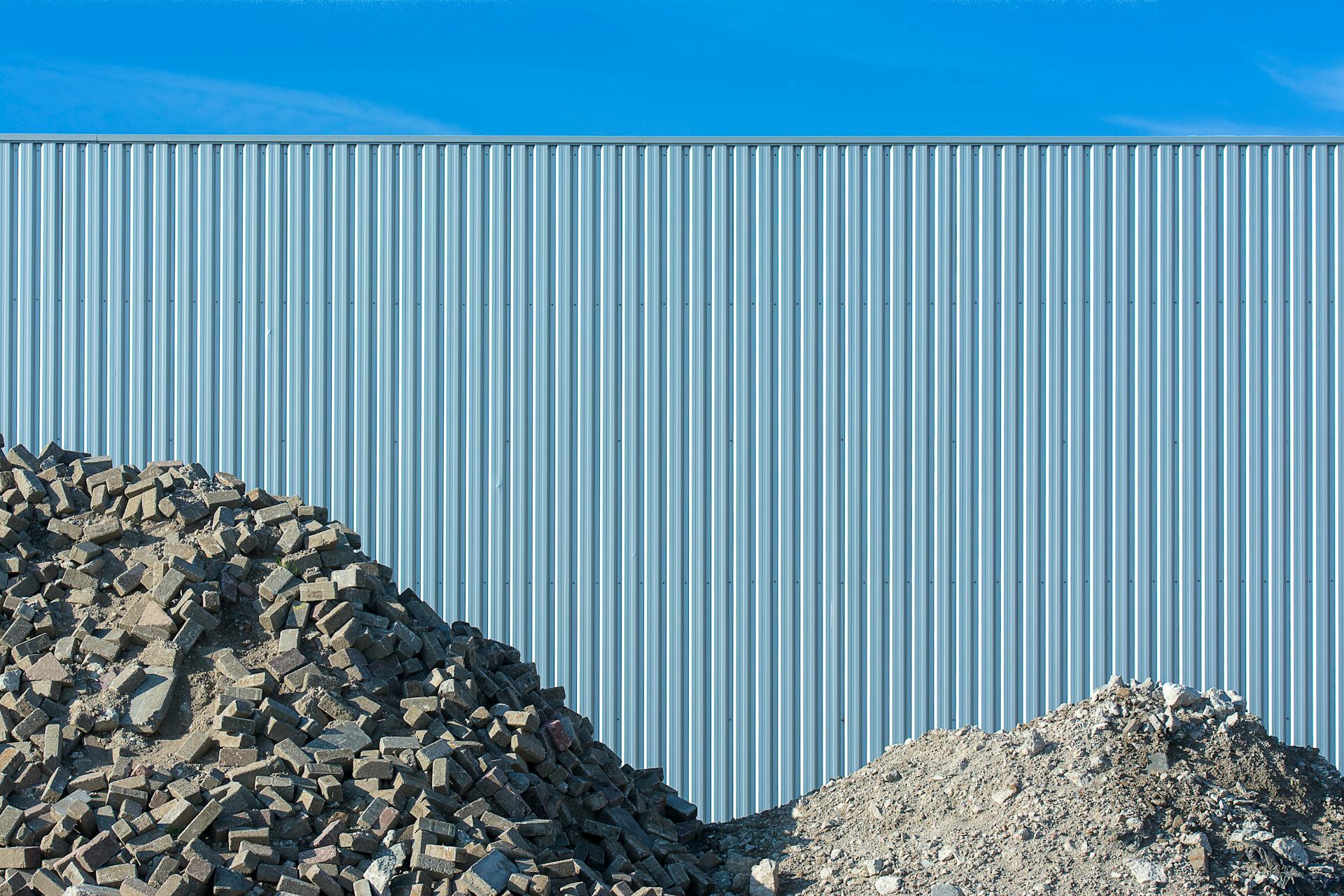 Piles of Rubble against Corrugated Metal Fence