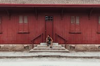 在巴西一栋乡村红色木制建筑的楼梯上，一名男子坐着，散发出复古的魅力