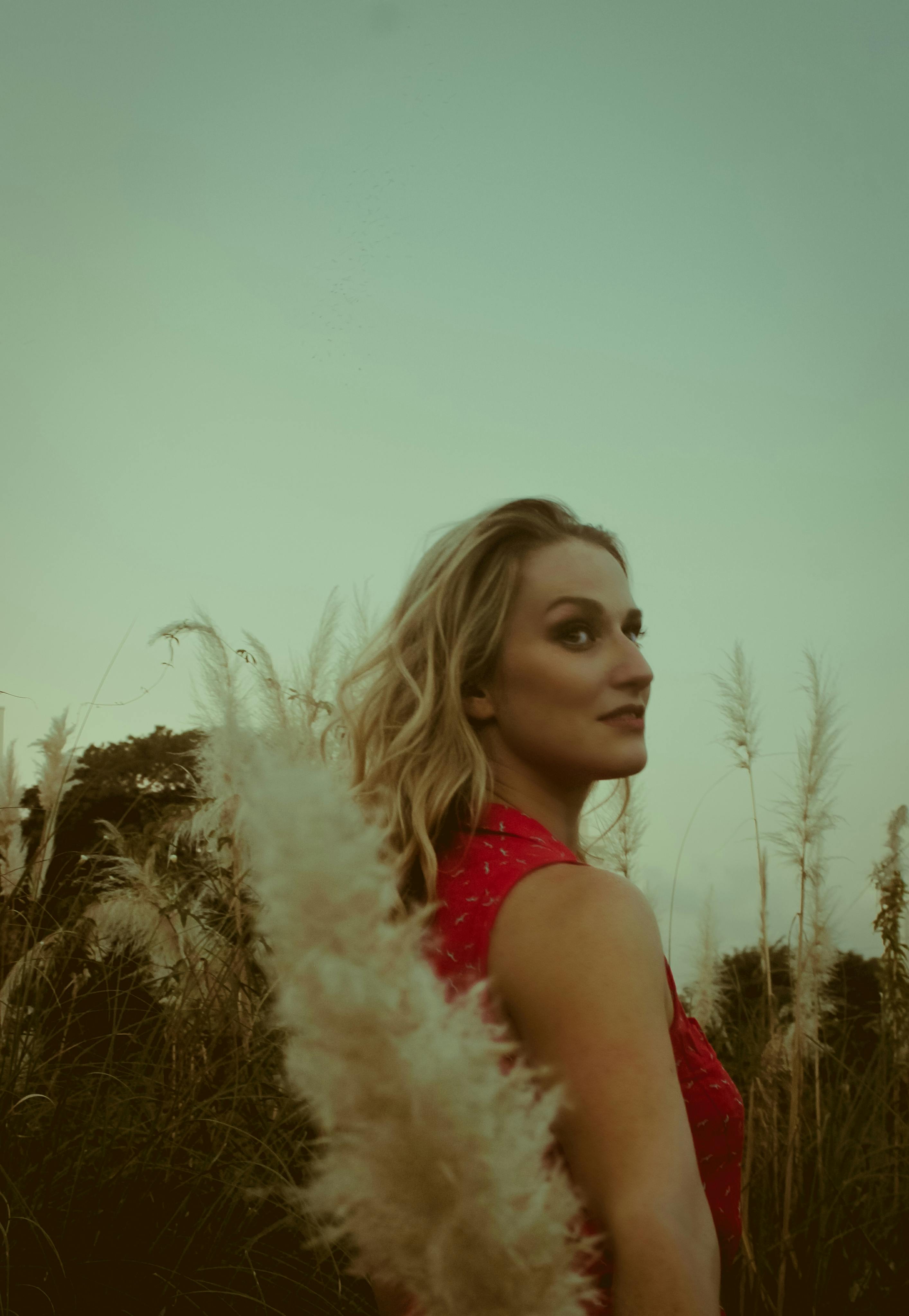 A woman in a red dress poses gracefully amidst tall grasses during sunset.