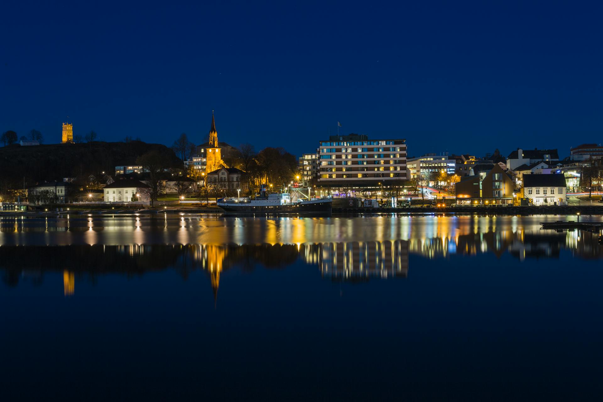 Illuminated Tønsberg waterfront with reflections on river at night.