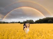 一位宁静的女子在充满活力的芥末花田中摆着姿势，头顶上悬着一道令人惊叹的双彩虹