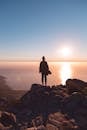 在开普敦的岩石悬崖上，一个人正欣赏着大海上令人惊叹的日落剪影