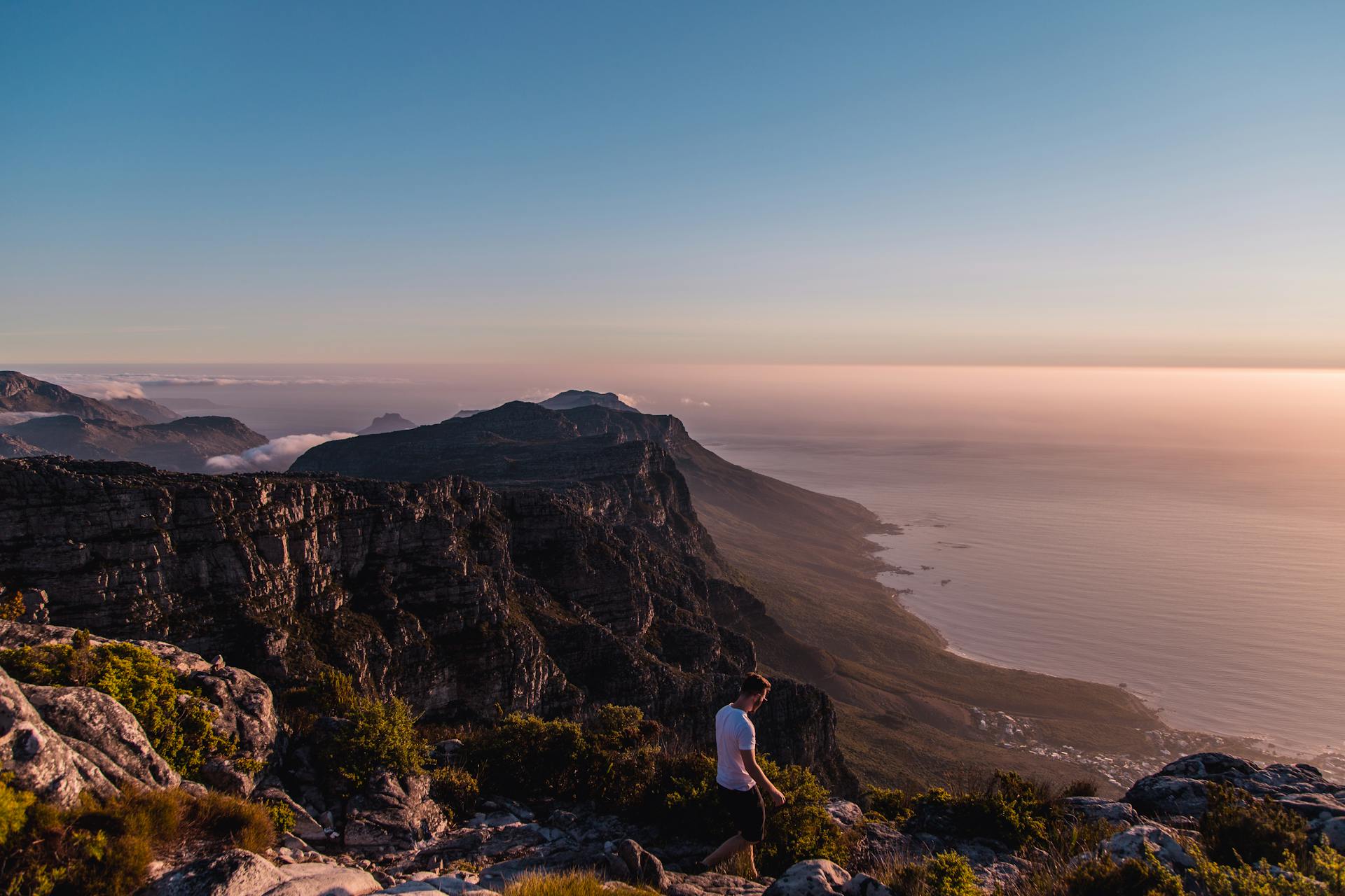 A solitary person walking on Table Mountain with a breathtaking sunset view over Cape Town, South Africa.