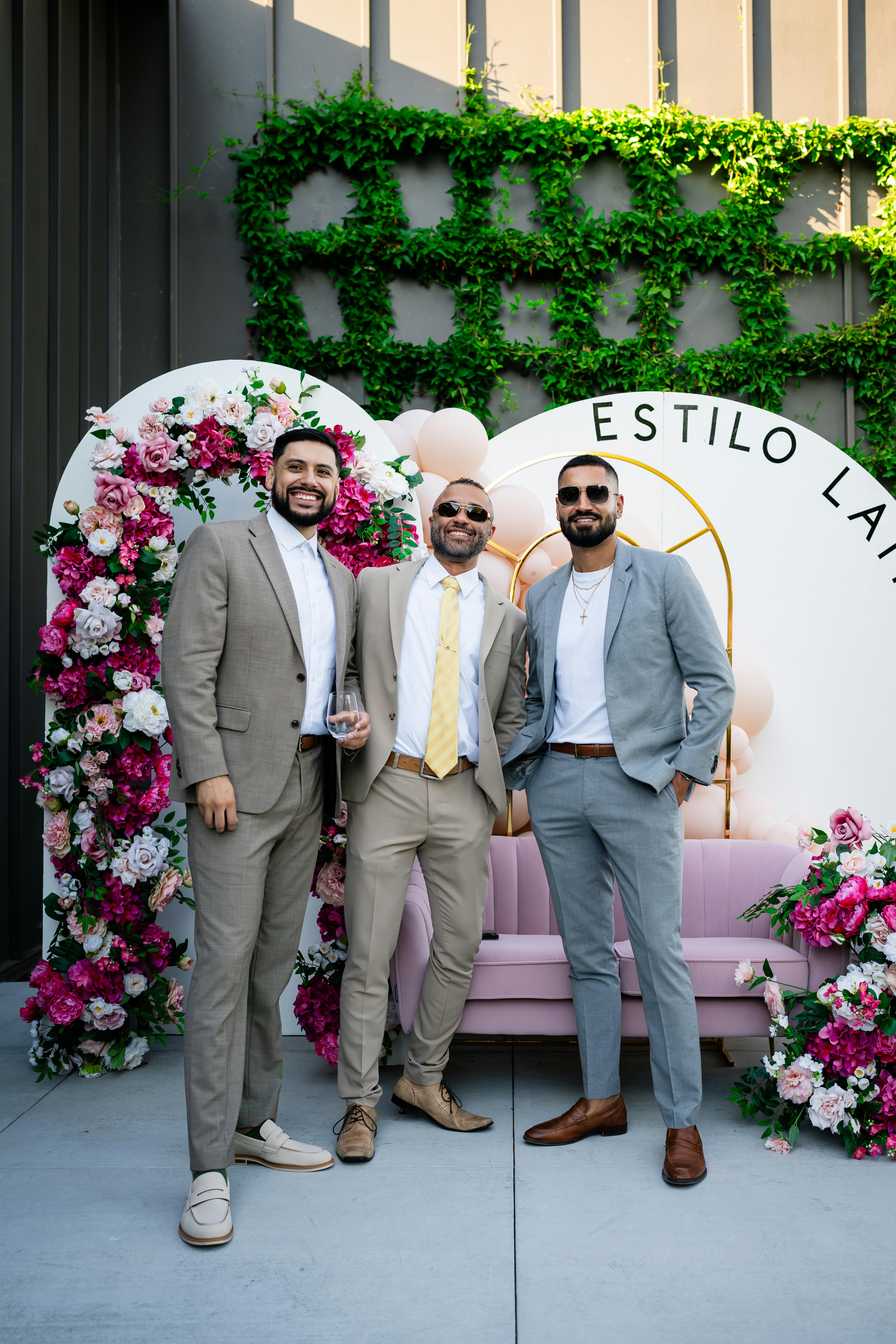 men in suits standing in front of a wall with flowers