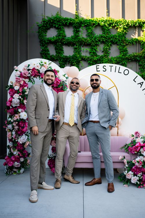 Free Three men in suits standing in front of a decorative floral backdrop at a celebration. Stock Photo