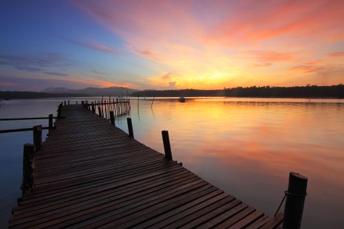 Free Tranquil sunrise over a calm lake with a rustic wooden pier stretching into the water. Stock Photo