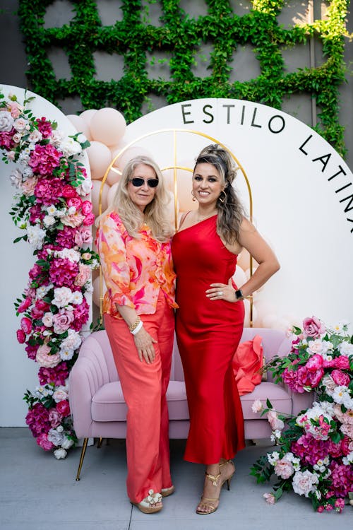Two women in red dresses standing next to a floral wall