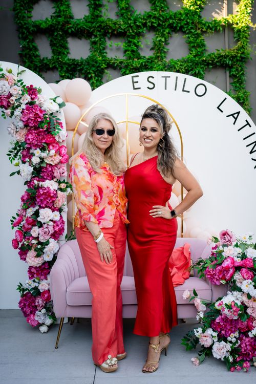 Free Mother and daughter standing together with a floral backdrop in vibrant fashion at a Latinx style event. Stock Photo