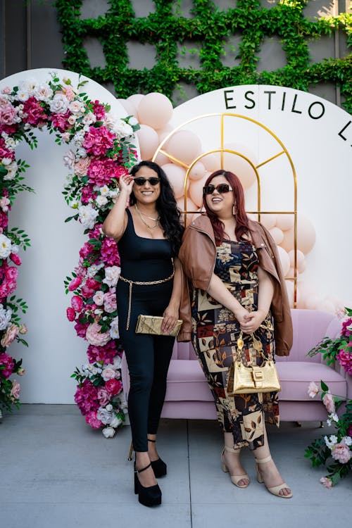 Two women posing for a photo in front of a floral backdrop