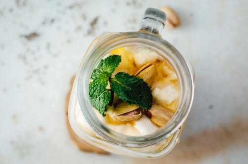 A glass jar filled with yogurt, nuts and mint