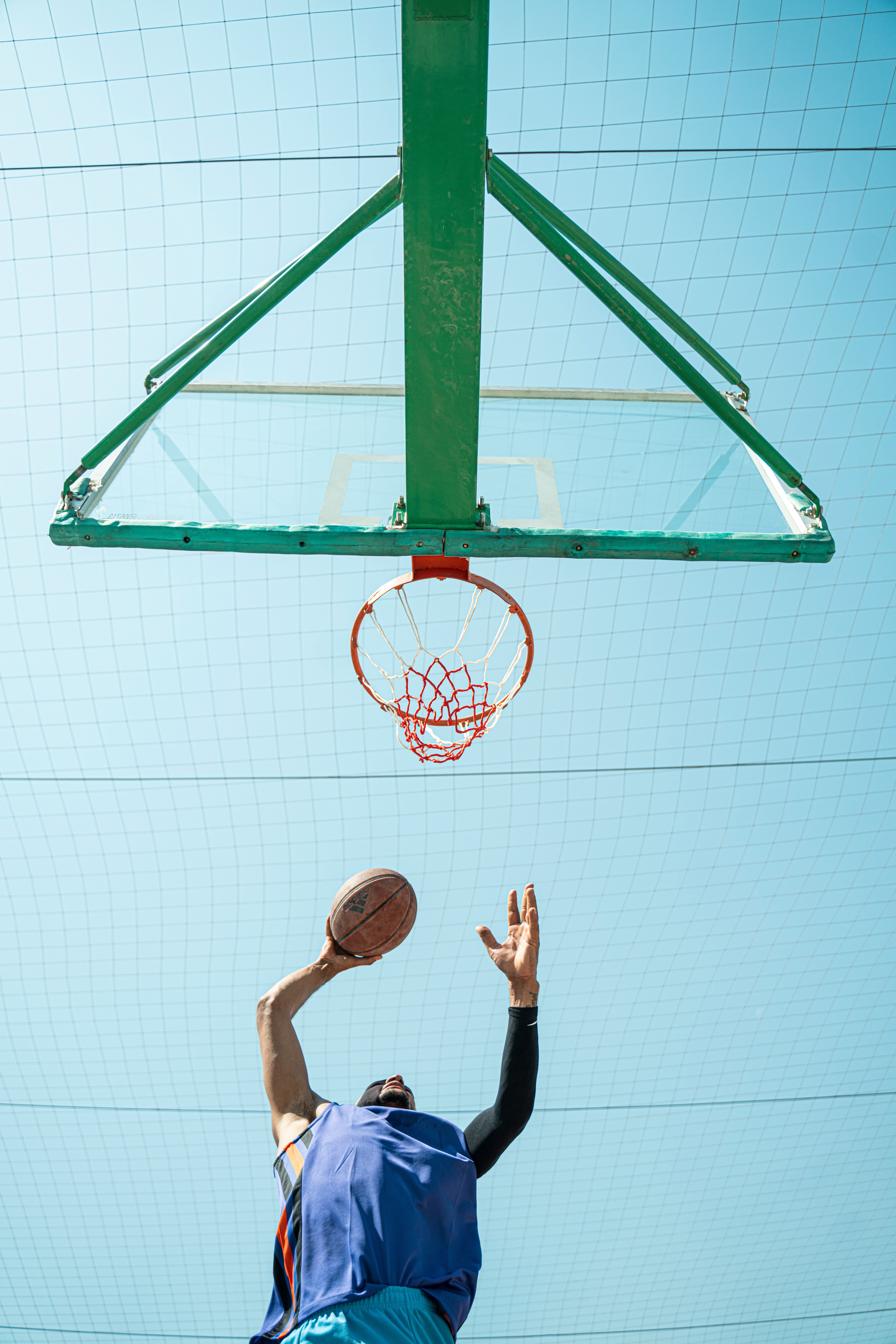 Low angle shot of a basketball player making a shot against a clear blue sky.