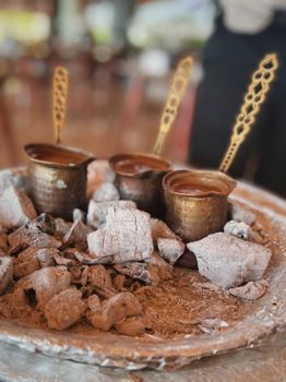 Close-up of Turkish coffee brewed in copper cezves on hot coals, showcasing traditional preparation.