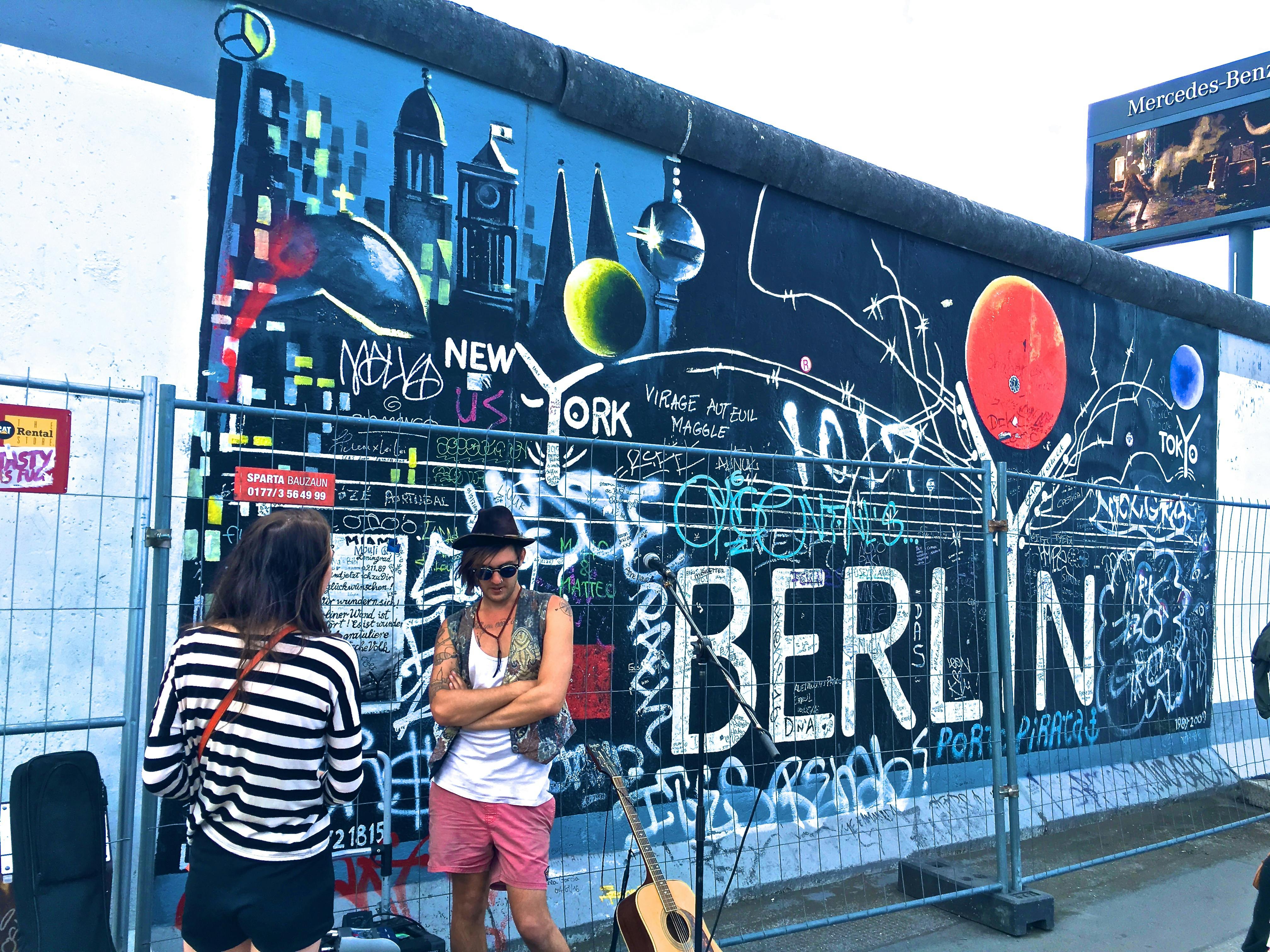 man wearing black waistcoat and white tank tops standing near a mural