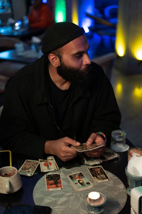 Free A man in a café setting reading tarot cards under soft ambient lighting. Stock Photo