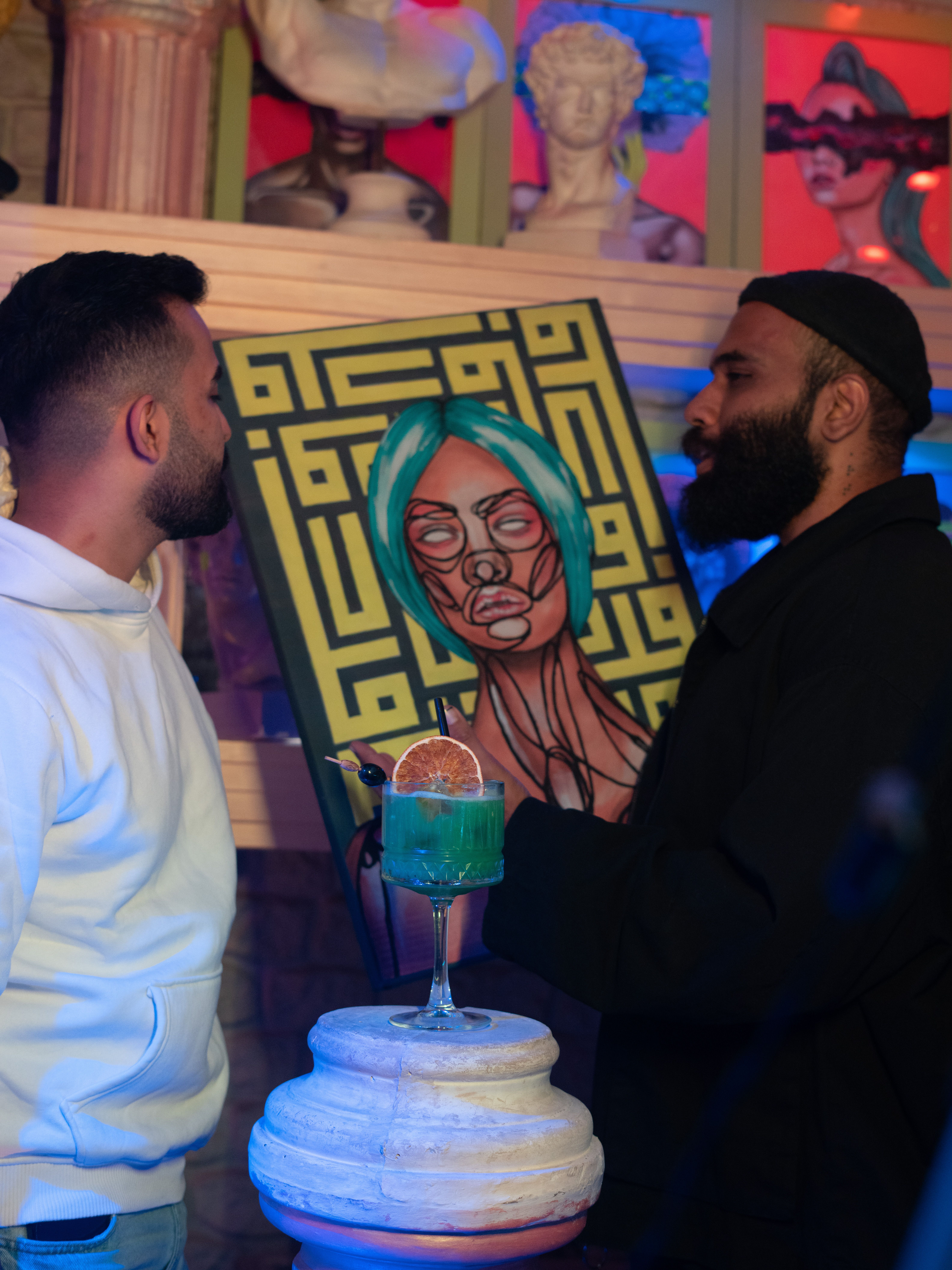Two men engaged in conversation about modern art in a vibrant gallery setting in Baghdad.