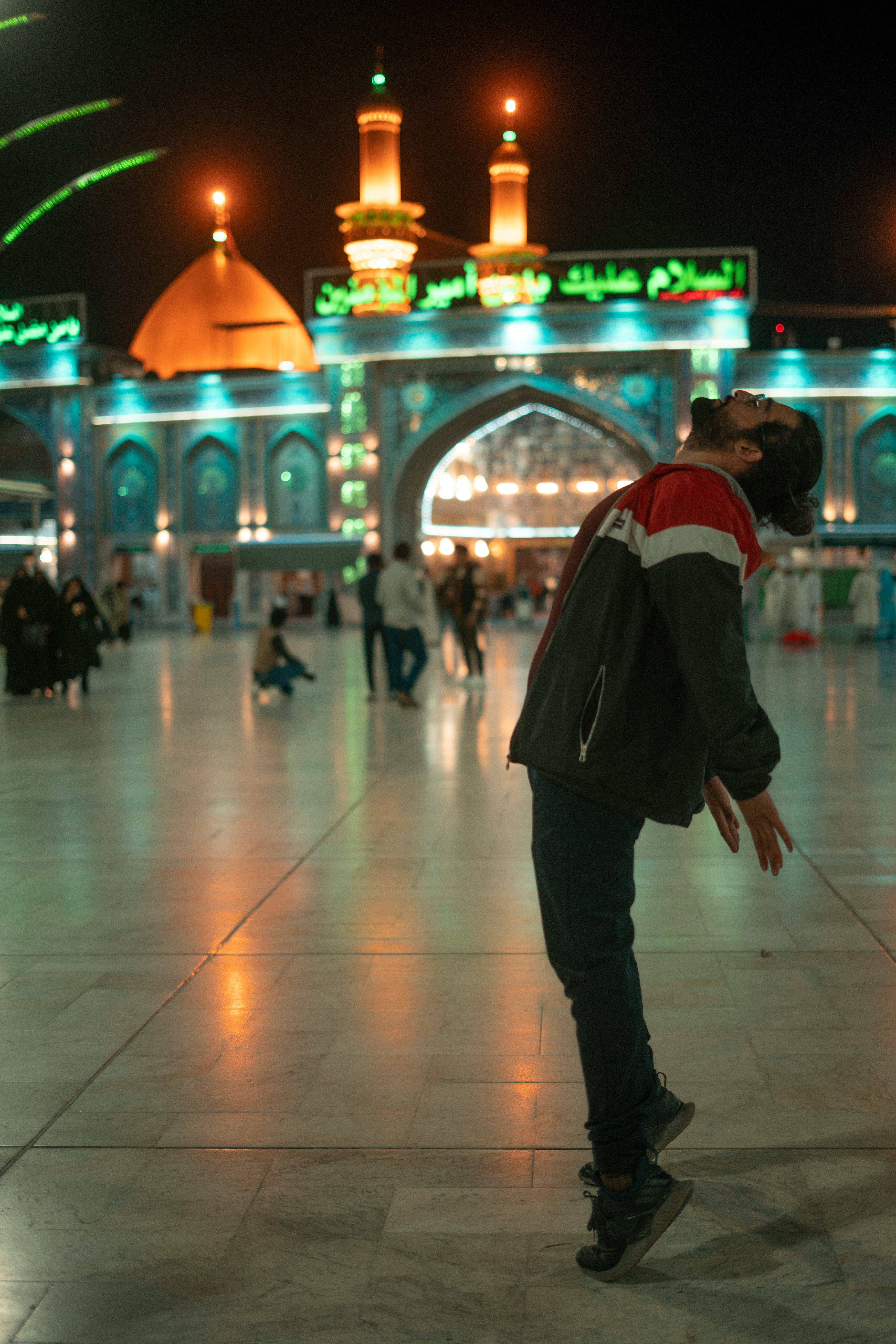 A man in a jacket poses dramatically at night near a mosque in Karbala, Iraq.
