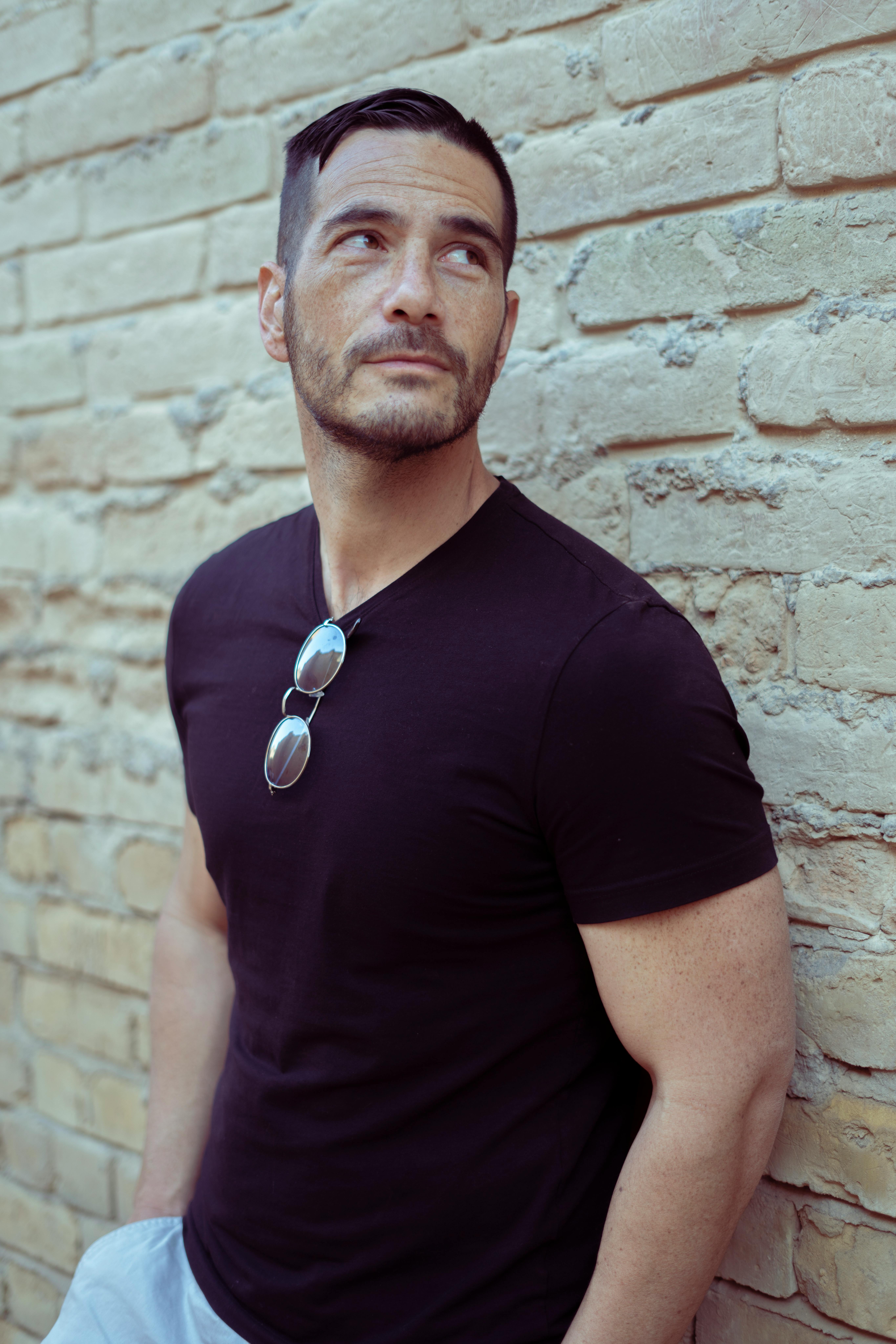 A casual portrait of a man in a black t-shirt leaning against a brick wall.